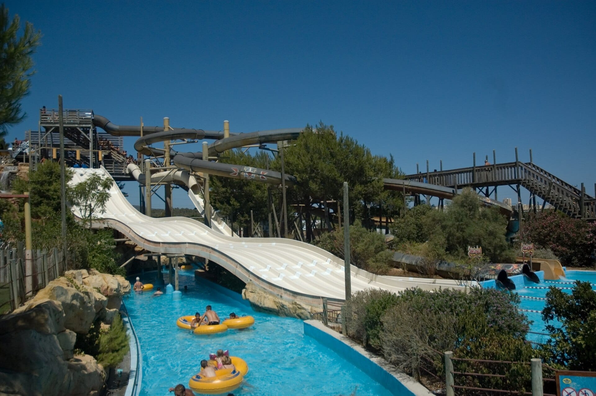 Ampi scivoli d'acqua e percorsi in tubo tortuosi al Western Water Park Magaluf, con famiglie su ciambelle gialle che godono di una giornata di sole.