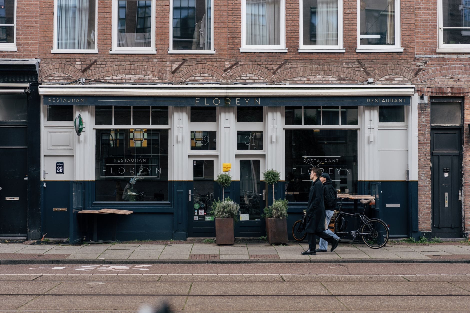 Vista de la calle del Restaurant Floreyn en Ámsterdam, un restaurante moderno con personas caminando frente a su fachada en una calle de la ciudad