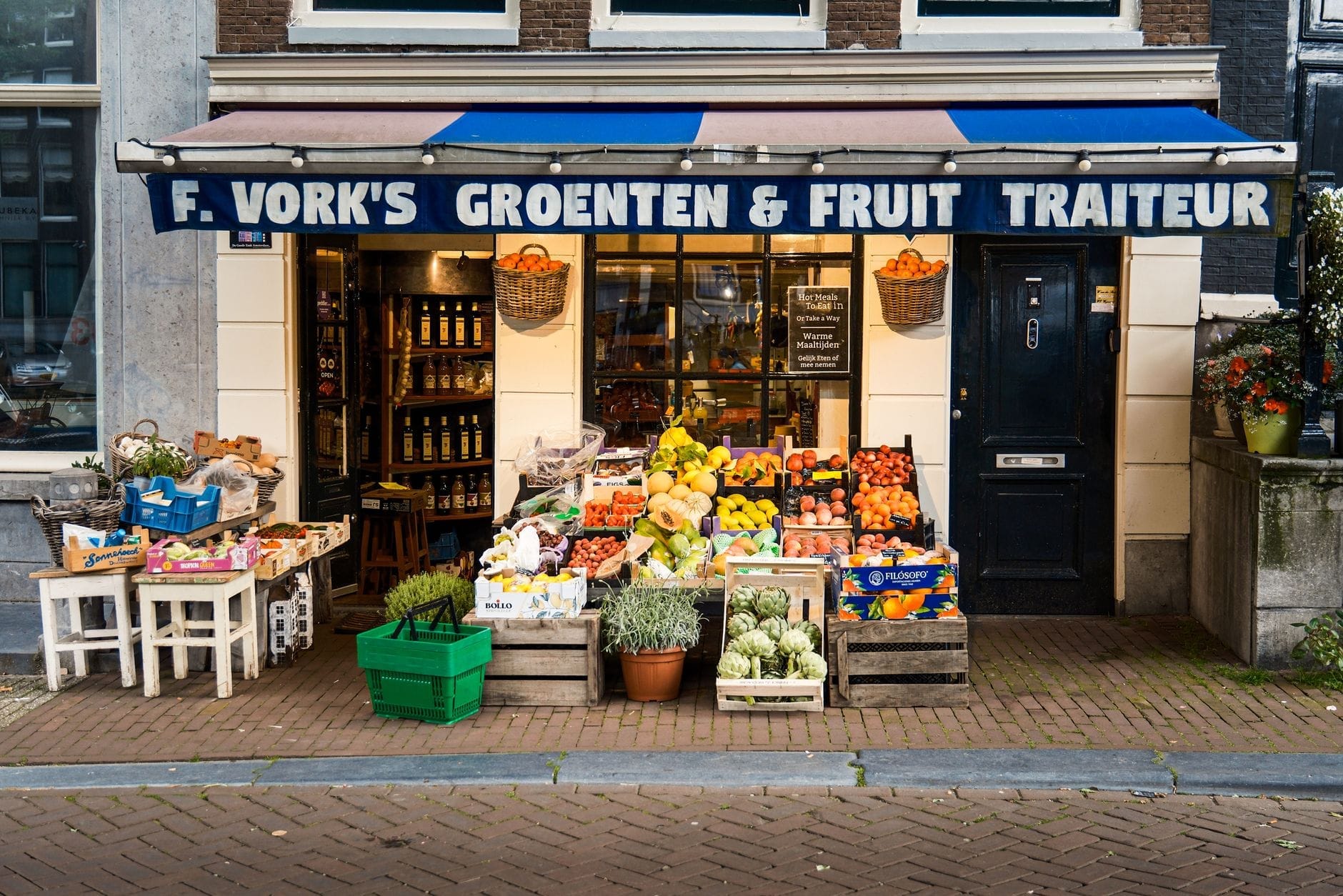 Fachada tradicional de una tienda en Amsterdam con el letrero 'Groenten & Fruit Traiteur' y productos frescos expuestos en la acera.