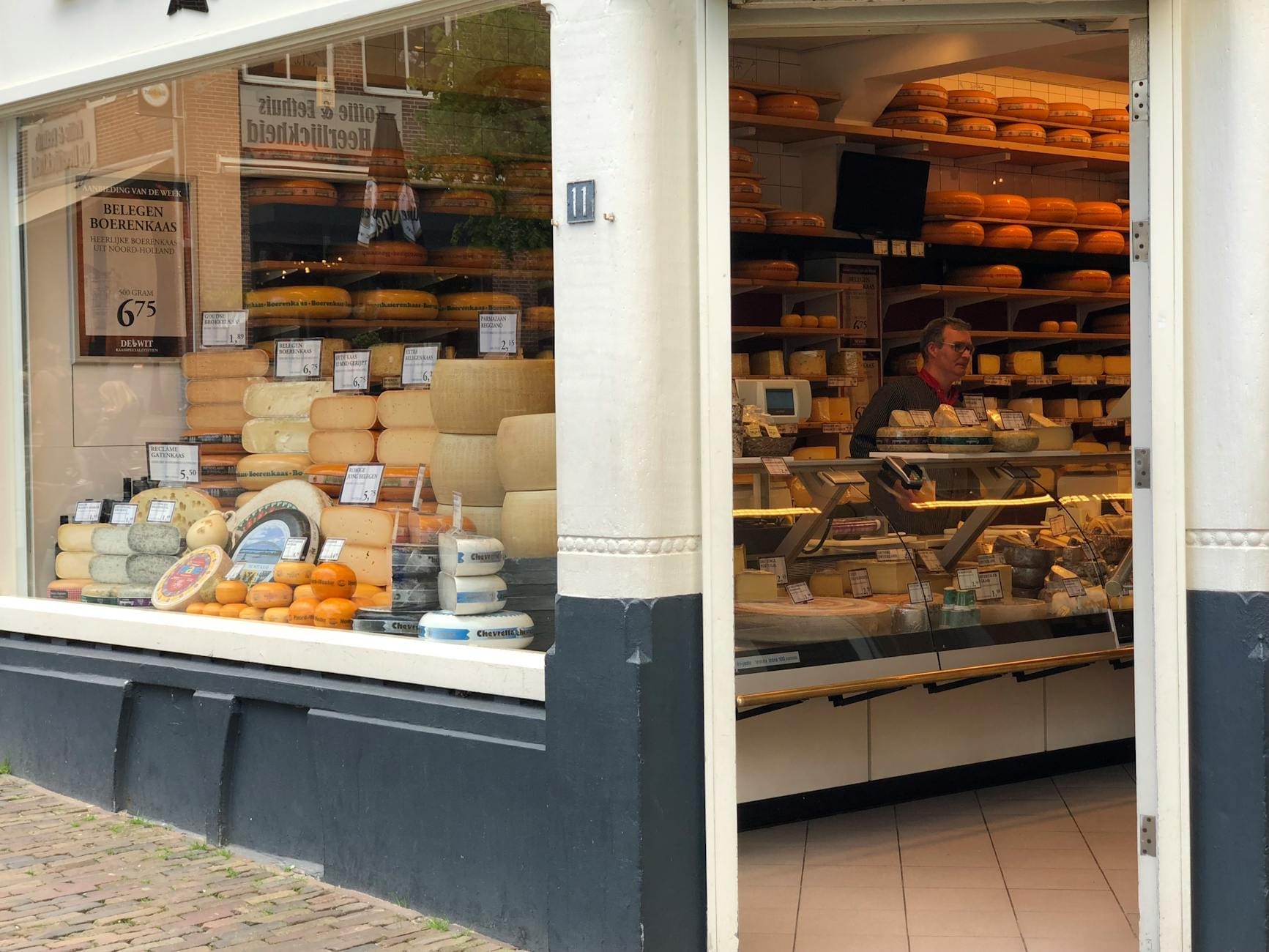 Vista interior de una tienda tradicional de quesos holandesa en Ámsterdam con estantes llenos de ruedas de queso redondas y una persona detrás del mostrador.
