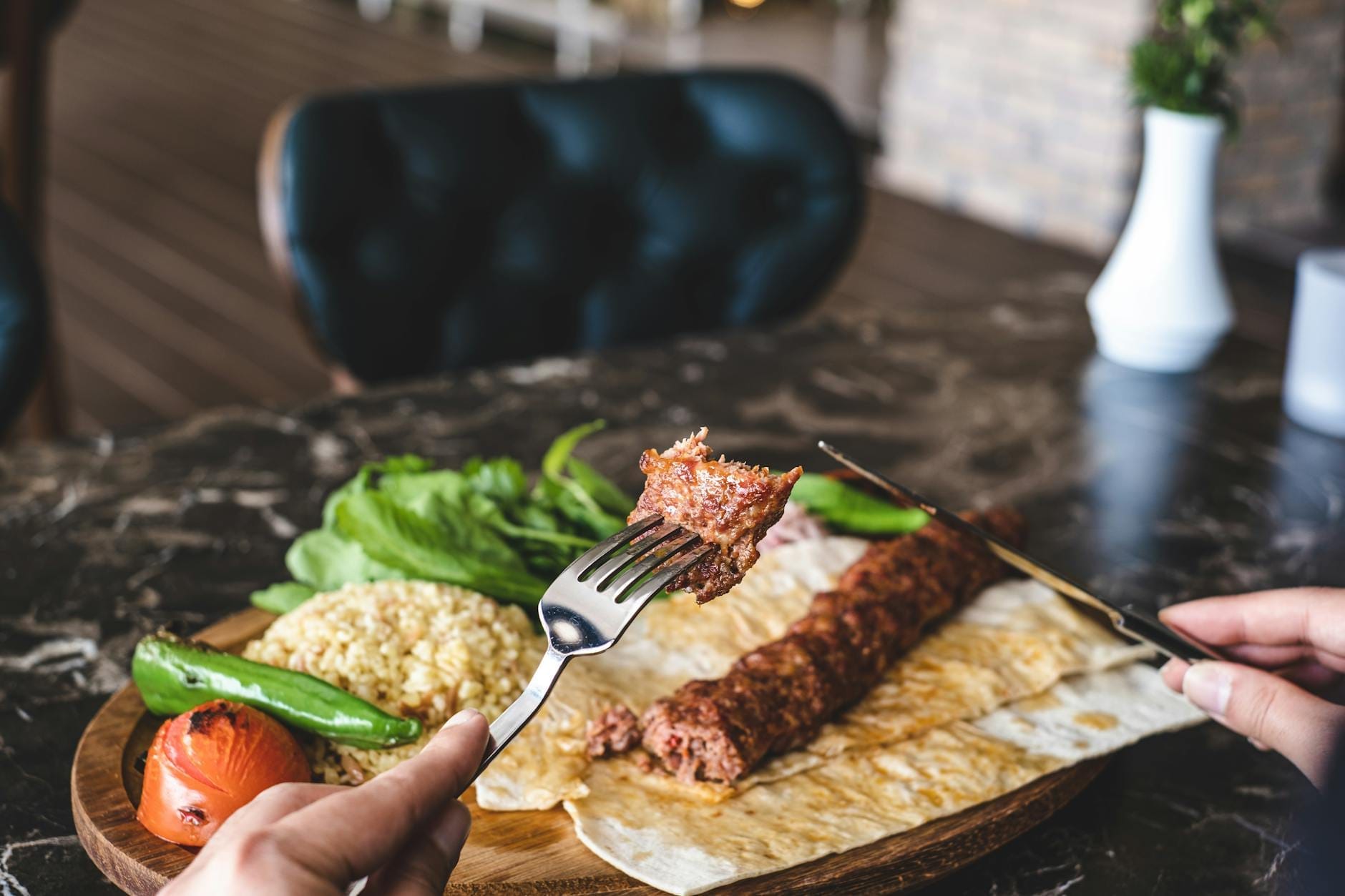 Close-up de um kebab turco tradicional servido com pão sírio, legumes grelhados, verduras e bulgur em uma bandeja de madeira num restaurante estiloso de Antalya.