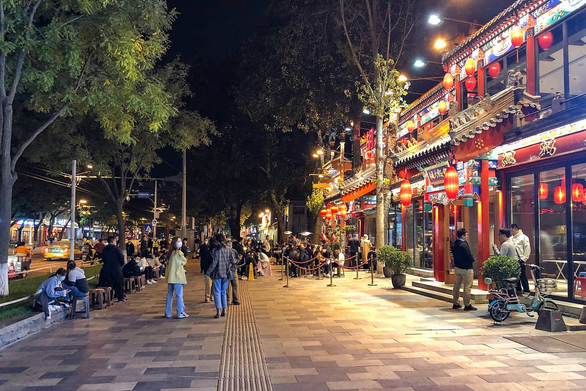 Lebhafte Nachtszene in einer belebten Straße in Beijing, gesäumt von bunten Restaurants und wartenden Menschen draußen.