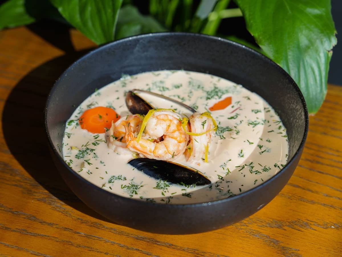 Eine Schüssel cremige Meeresfrüchte-Chowder garniert mit Garnelen, Muscheln, Kräutern und Gemüse auf einem Holztisch.