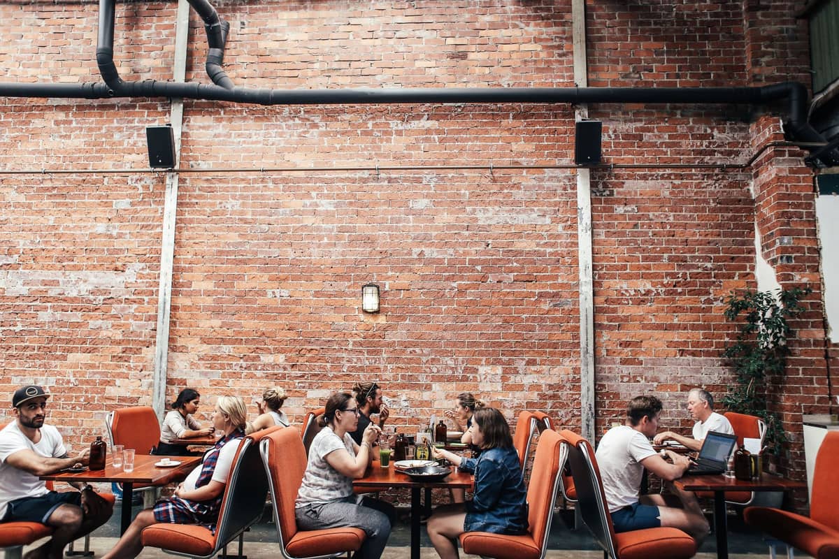 Ludzie jedzący w restauracji na świeżym powietrzu z ceglanymi ścianami, oddający klimat tętniącej życiem sceny restauracyjnej Brisbane.