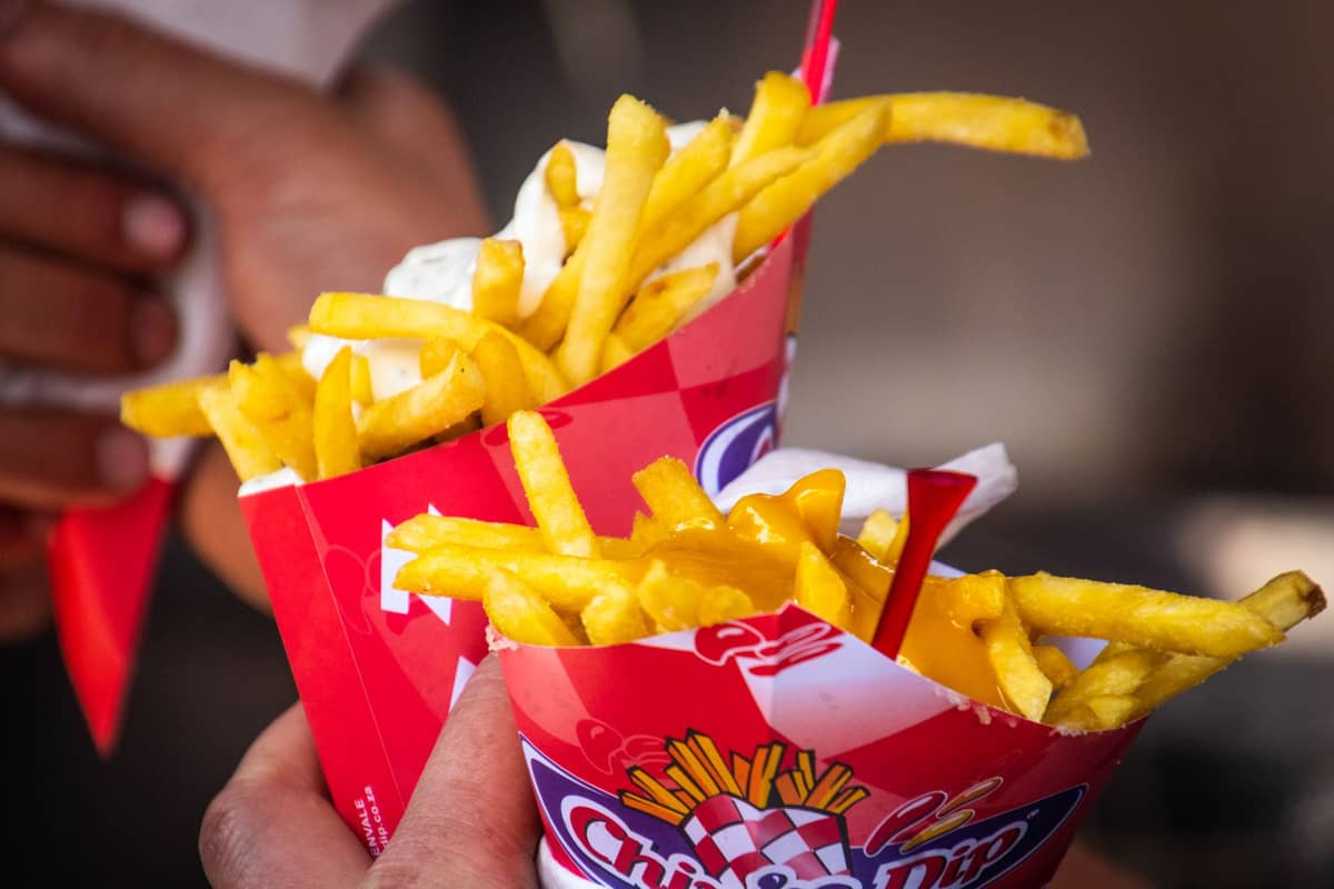 Two hands holding paper cones filled with golden fries and topped with sauce, typical Belgian street food style.