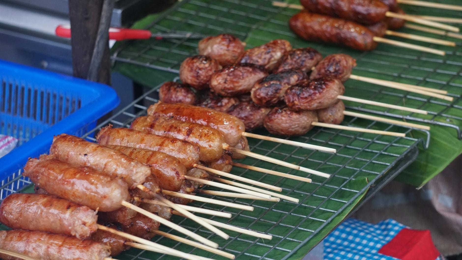 Salchichas tradicionales del norte de Tailandia y otras carnes en brocheta sobre una parrilla de comida callejera en un puesto del mercado de Chiang Mai.