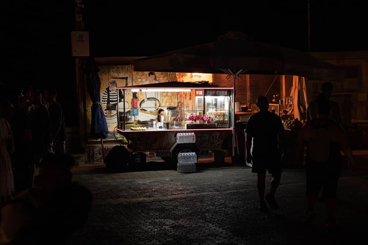 Beleuchteter Essensstand im Freien bei Nacht mit vorbeigehenden Menschen, der die lebhafte nächtliche Street-Food-Kultur von Doha einfängt.
