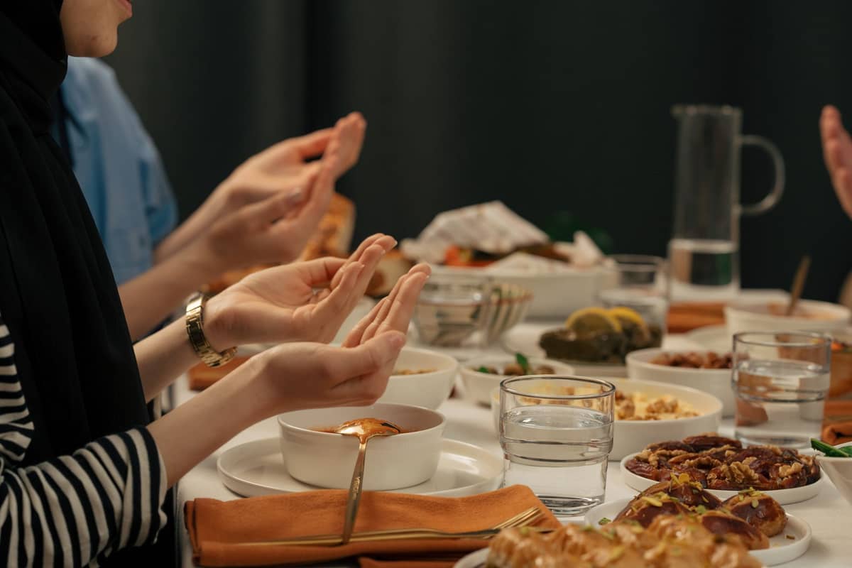 Menschen beten über einem Tisch mit verschiedenen Speisen vor dem Fastenbrechen und zeigen die traditionelle Ramadan-Iftar-Mahlzeitenatmosphäre.