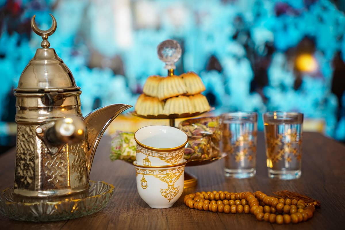 Traditionelle arabische Kaffeekanne, Finjan-Tassen, Süßigkeiten und Wassergläser auf einem Tisch, die für emiratische Getränke und Snacks stehen.