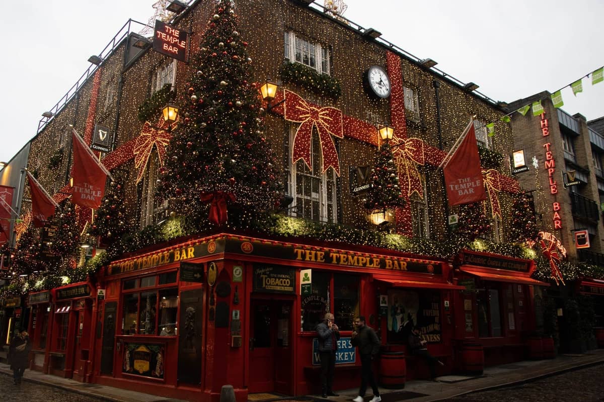 Vista esterna del pub The Temple Bar a Dublino decorato con luci e ornamenti natalizi, con pedoni su una strada acciottolata.