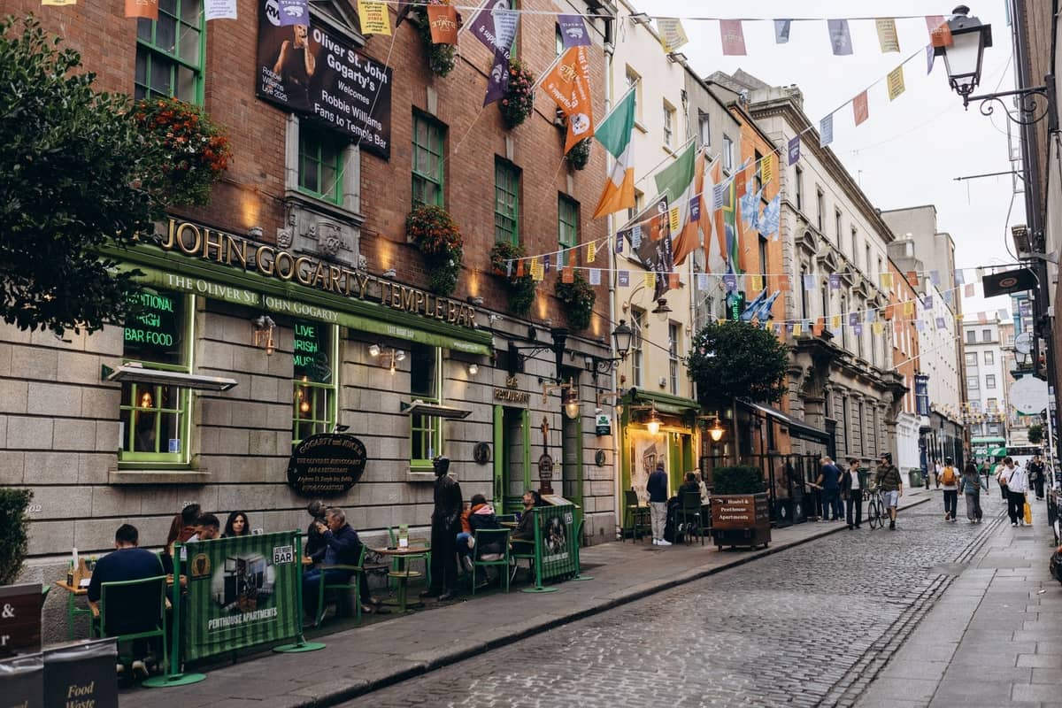 Vivace scena di strada a Dublino con pub, ristoranti all'aperto, bandiere e persone a Temple Bar, che cattura l'atmosfera dei quartieri gastronomici più popolari.