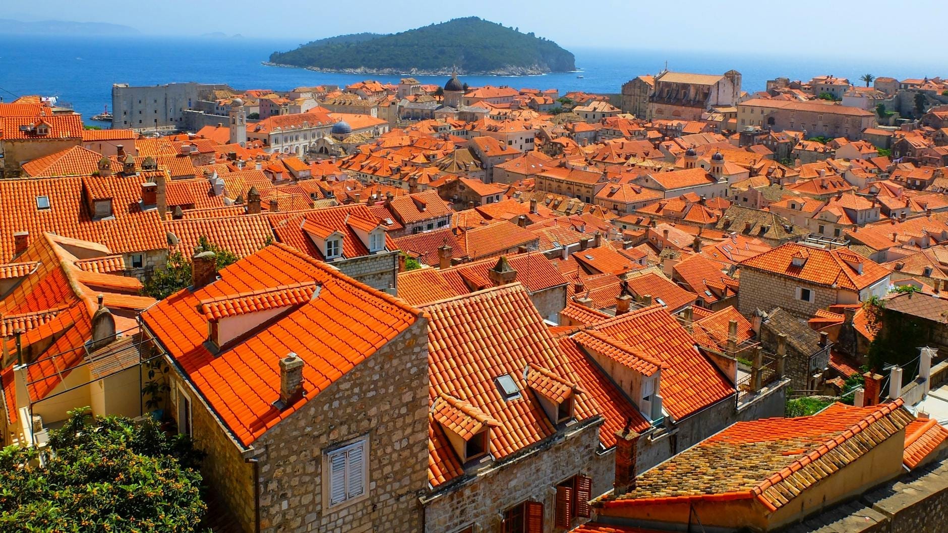 Vista panorámica del casco antiguo de Dubrovnik con sus tejados rojos, edificios de piedra y el mar Adriático al fondo en un día soleado y despejado.