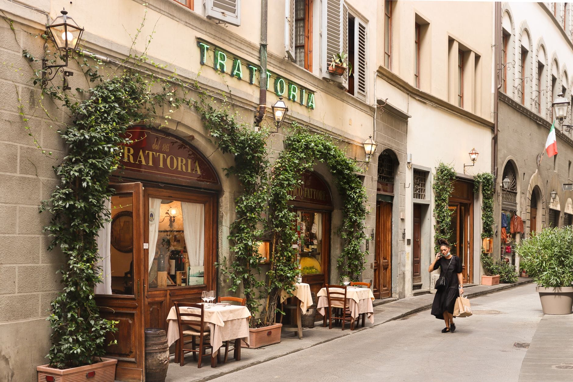 วิวถนนของ trattoria แบบคลาสสิกในเมือง Florence ที่มีไม้เลื้อยบนหน้าอาคาร โต๊ะนั่งกลางแจ้ง และมีคนเดินผ่าน
