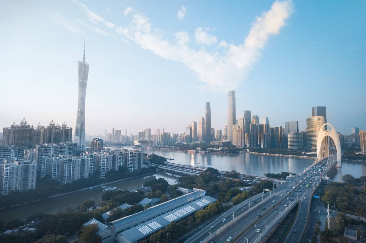 Wide view of Guangzhou city skyline with the Canton Tower, modern skyscrapers, and the iconic Liede Bridge over the Pearl River in daylight.