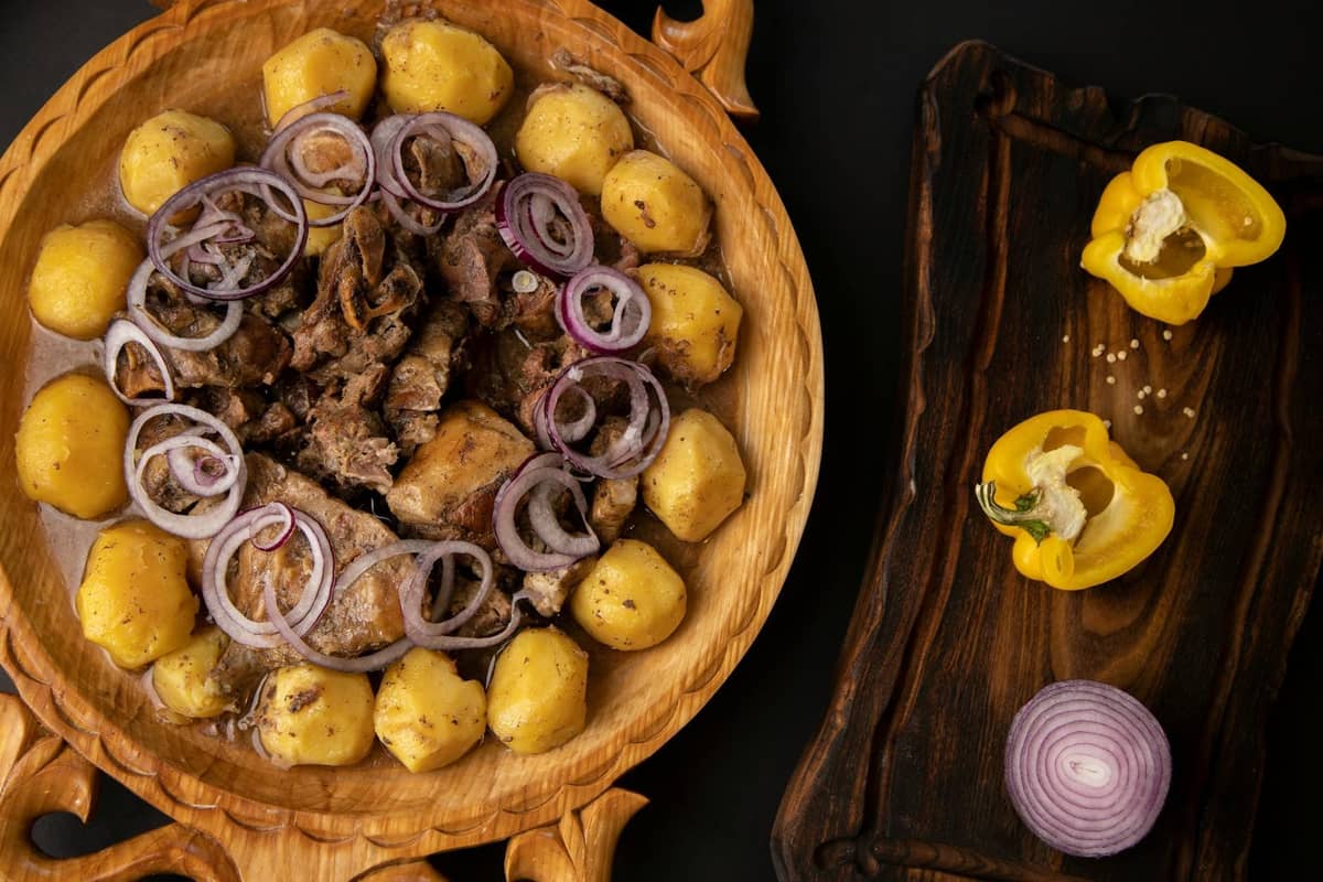 Wooden platter with slow-cooked meat, potatoes, and sliced onions arranged neatly, evoking a rustic Montenegrin mountain dish.