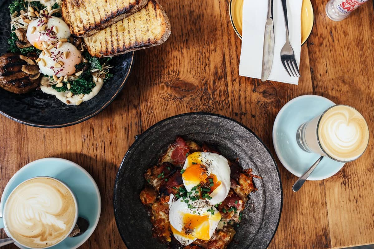Brunch w stylu Melbourne z jajkami w koszulkach, tostami i kawą specialty podanymi na drewnianym stole w kawiarni