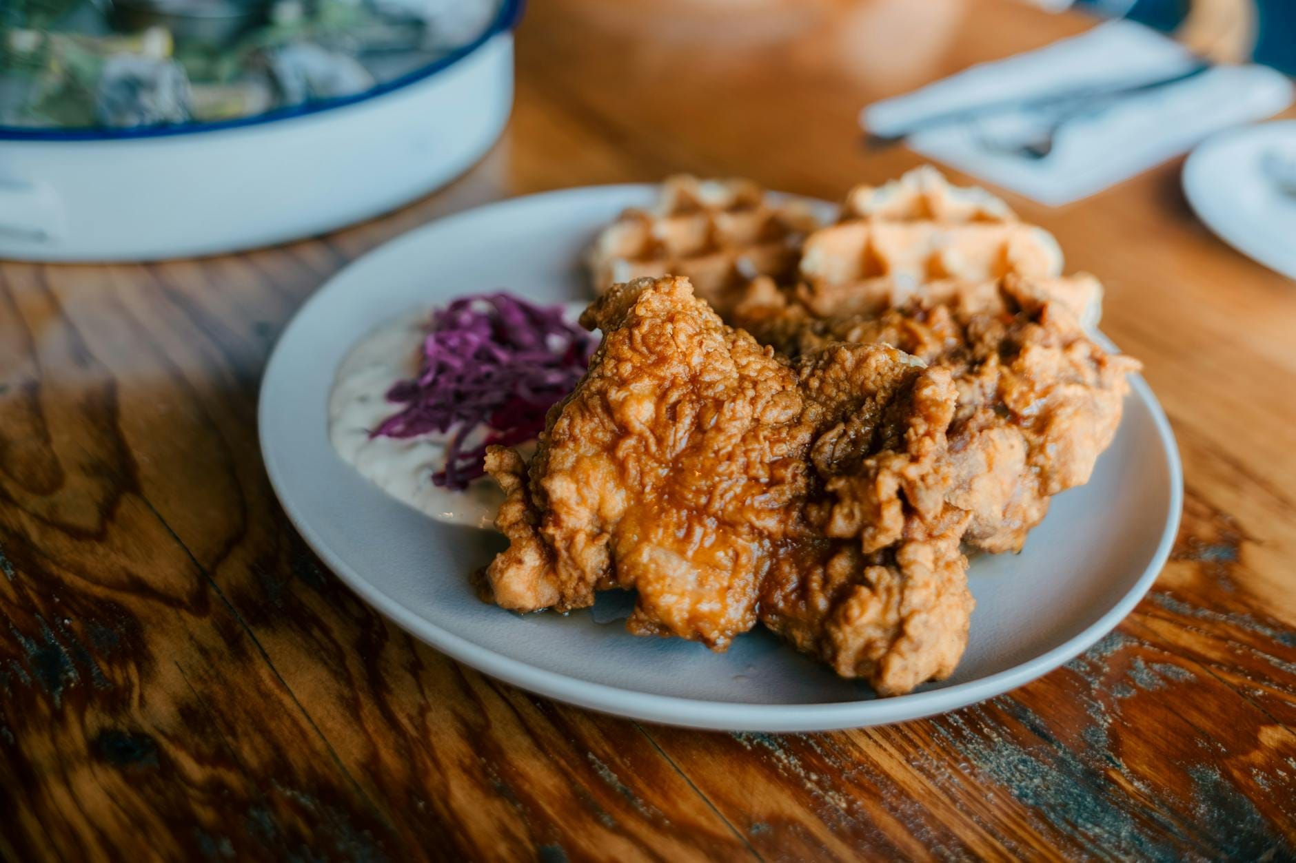 Primer plano de un plato de pollo frito crujiente y waffles dorados servidos con ensalada cremosa y salsa, clásica comida reconfortante sureña sobre una mesa rústica de madera.