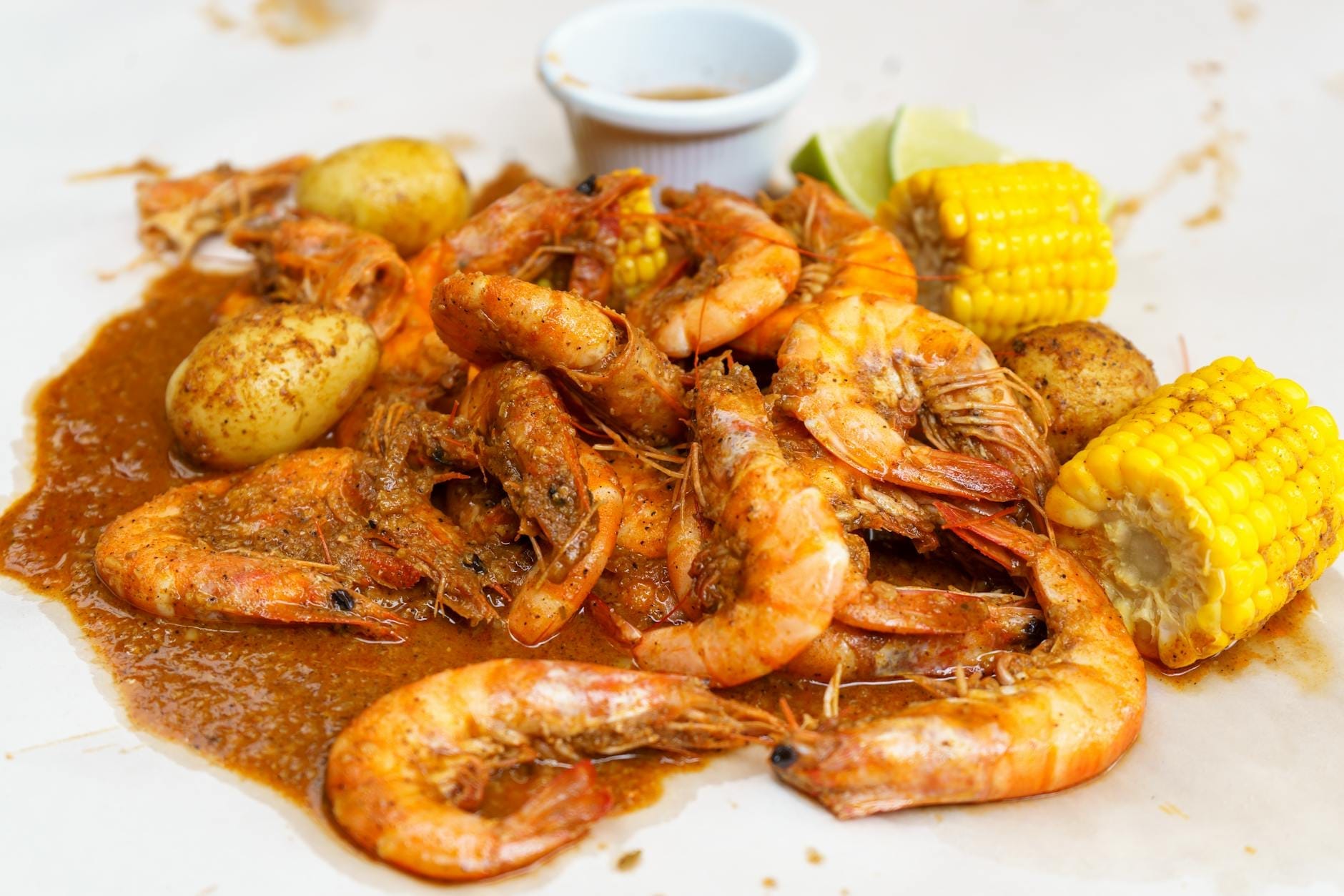 Close-up de um seafood boil Cajun com camarões, batatas, espiga de milho e molho sobre uma mesa branca.