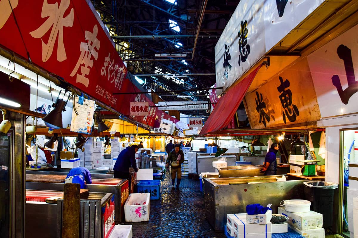 Inside an Osaka seafood market with stalls selling fresh fish, Japanese signage overhead, and shoppers browsing the vibrant displays.