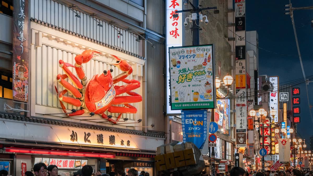 Night street scene in Dotonbori, Osaka with a giant crab restaurant sign, colorful neon signs, and crowds of people enjoying the vibrant food district.