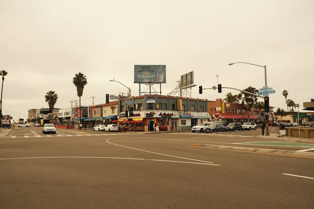 Weitläufige Ansicht einer Straßenecke in San Diego mit niedrigen bunten Gebäuden, kleinen Restaurants, Palmen, Autos und Fußgängern, die das kulinarische Flair eines Viertels vermittelt.