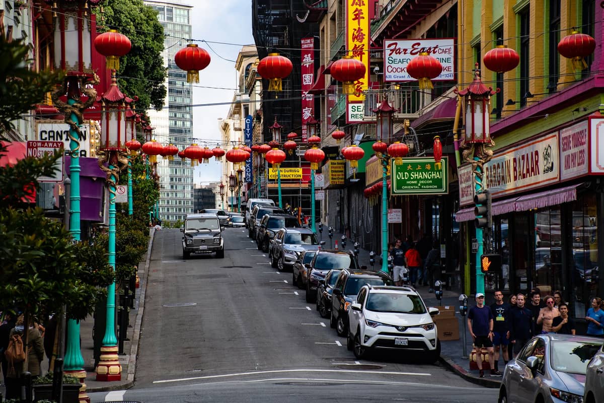 A street in San Francisco's Chinatown lined with colorful lanterns and restaurant signs, capturing the neighborhood's vibrant food culture.