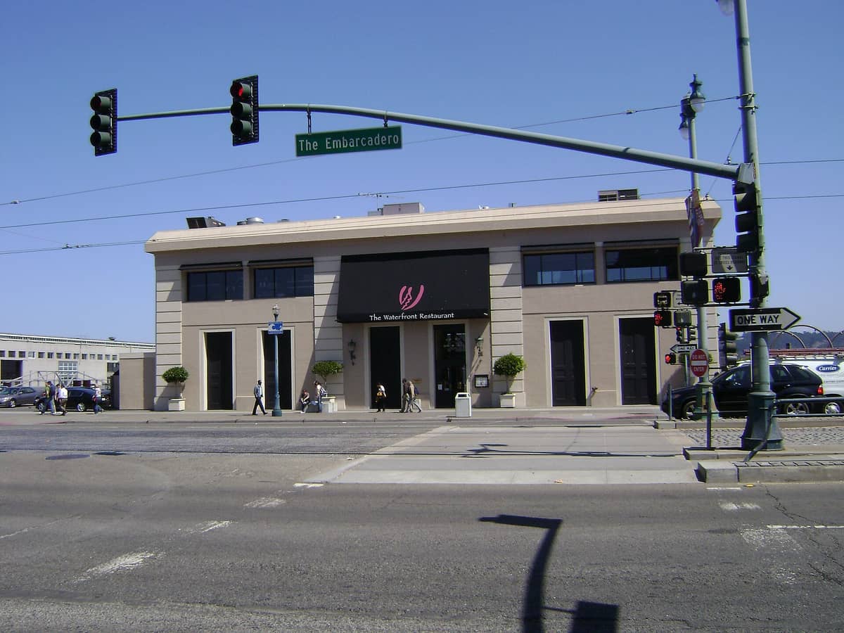 Street view of The Waterfront Restaurant on The Embarcadero in San Francisco, with pedestrians and street signs visible.