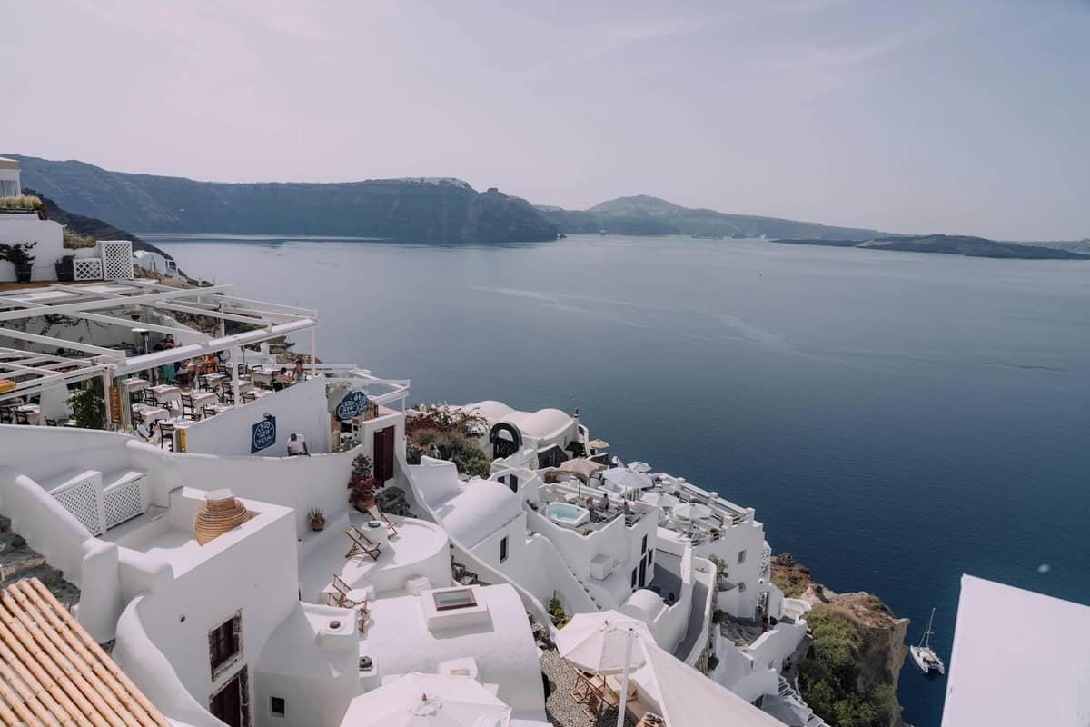 Outdoor restaurants with whitewashed terraces overlooking the Santorini caldera and sea, with tables set for dining and beautiful panoramic views.