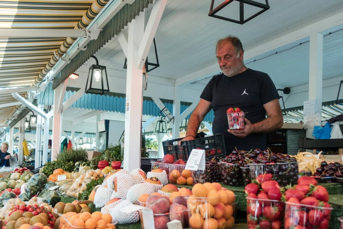 Un marchand de marché arrange des fruits frais sur un étal animé en plein air à Split, présentant des pêches, des cerises et d'autres produits locaux typiques de la cuisine dalmate.