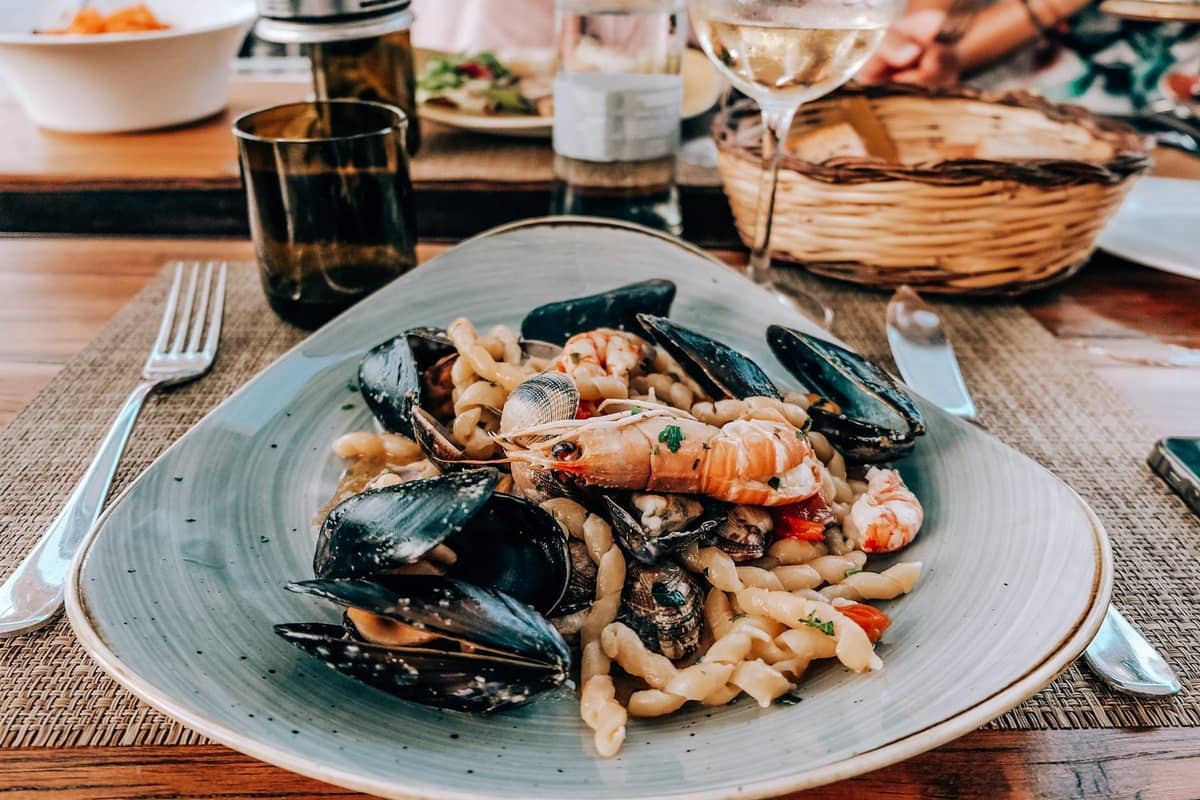 Une assiette de pâtes aux fruits de mer avec des moules et des crevettes servie sur une table de restaurant avec du vin et du pain.