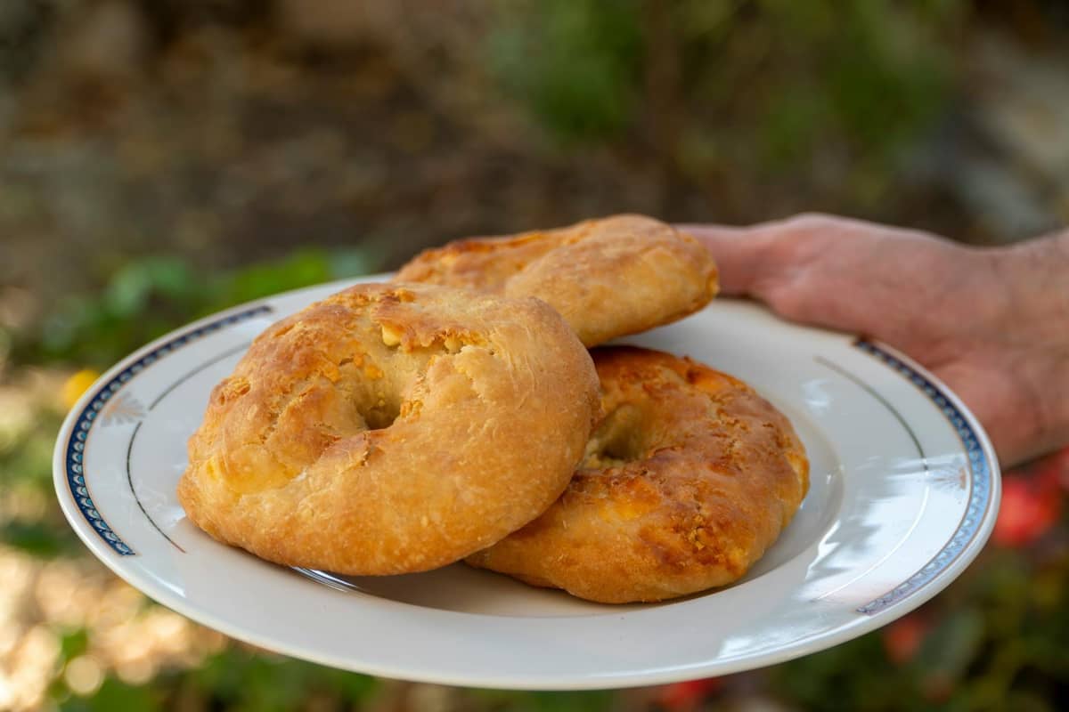 Trois pains plats ronds et rustiques à la croûte dorée servis sur une assiette blanche, tenus en extérieur, représentant le pain traditionnel dalmate.