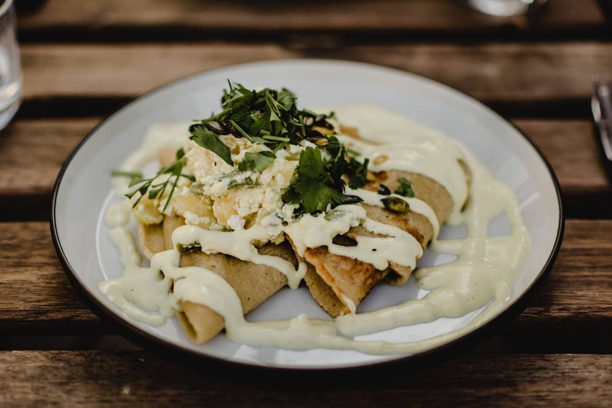 Ein Teller estnischer herzhafter Pfannkuchen, garniert mit Kräutern und cremiger Sauce, serviert auf einem rustikalen Holztisch im natürlichen Licht.