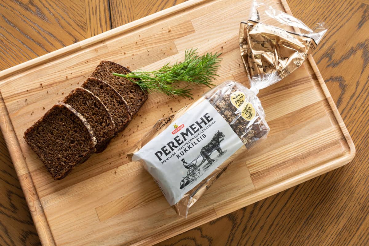 Ein aufgeschnittenes verpacktes dunkles estnisches Roggenbrot mit der Aufschrift 'PEREMEHE RUKKILEIB' auf einem Holzschneidebrett mit einem Dillzweig.