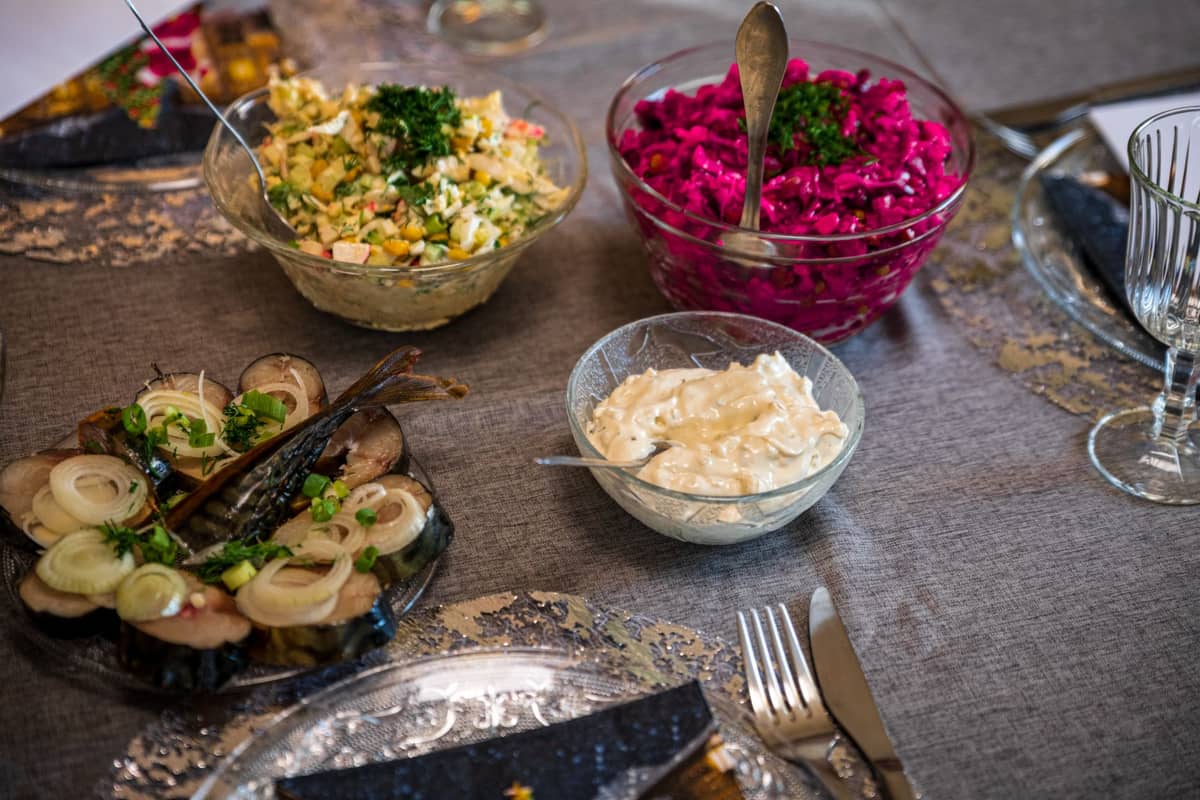 Tischaufstellung mit traditionellen estnischen Speisen, darunter Hering mit Zwiebeln, Rote-Bete-Salat, Kartoffelsalat und ein cremiger Dip in Glasschüsseln.