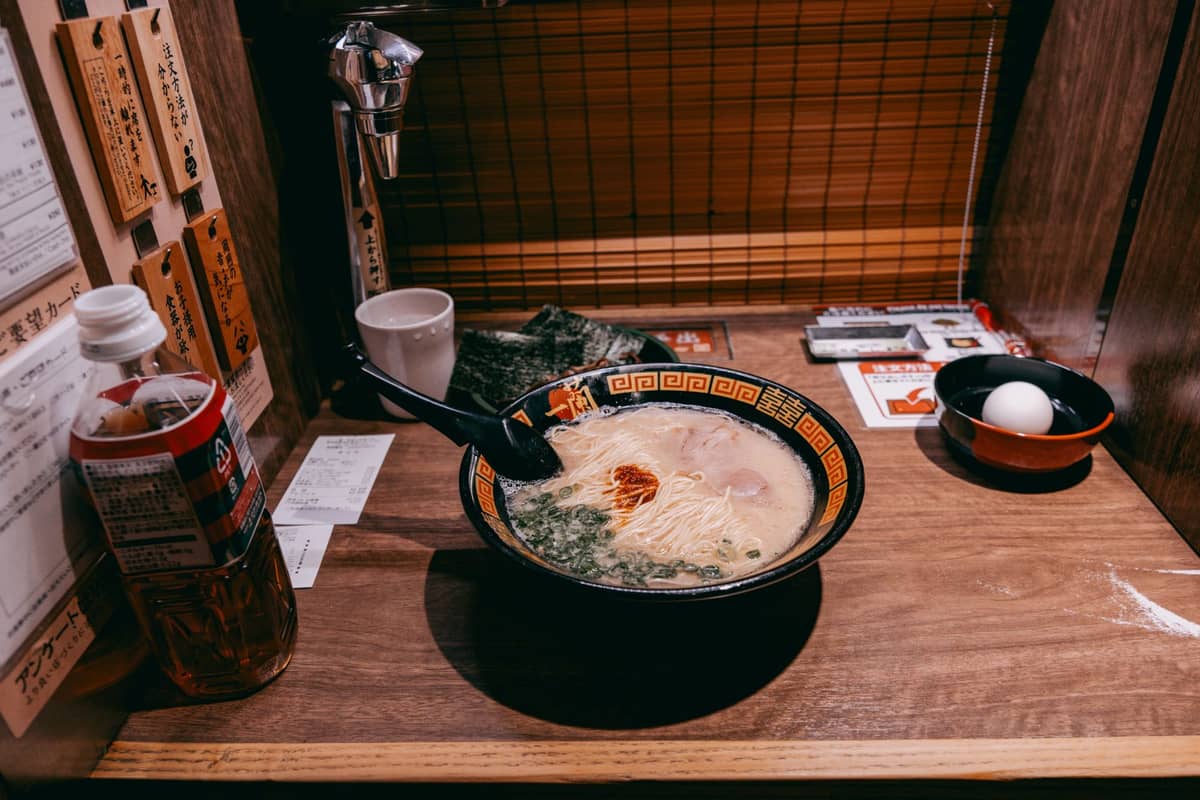 A bowl of ramen with toppings sits on a wooden counter at a solo dining booth in a Tokyo ramen restaurant, showcasing a classic Japanese dish.