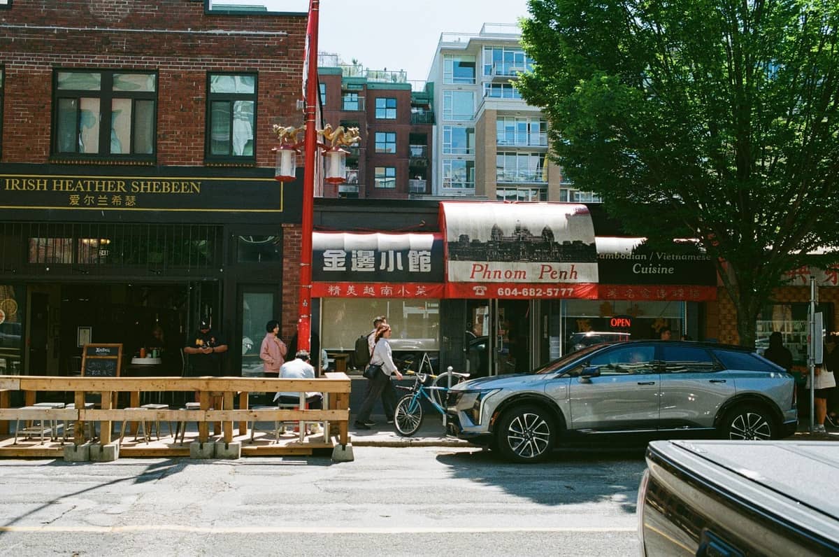 Straßenszene mit einer Mischung aus chinesischen und anderen Restaurants, vorbeigehenden Menschen und modernen Gebäuden im Hintergrund, typisch für Metro Vancouver.