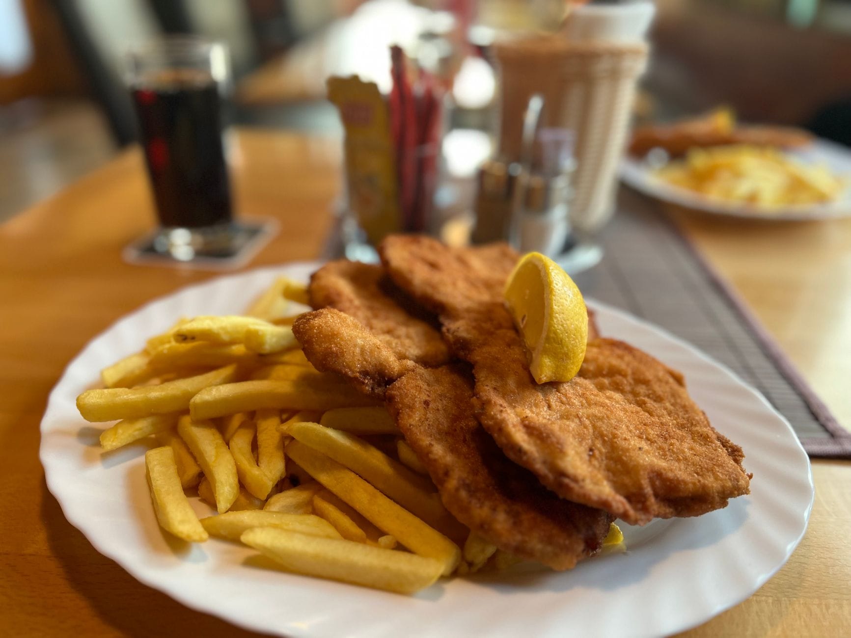 Ein Teller Wiener Schnitzel mit Pommes frites und einer Zitronenspalte in einem gemütlichen Restaurant.