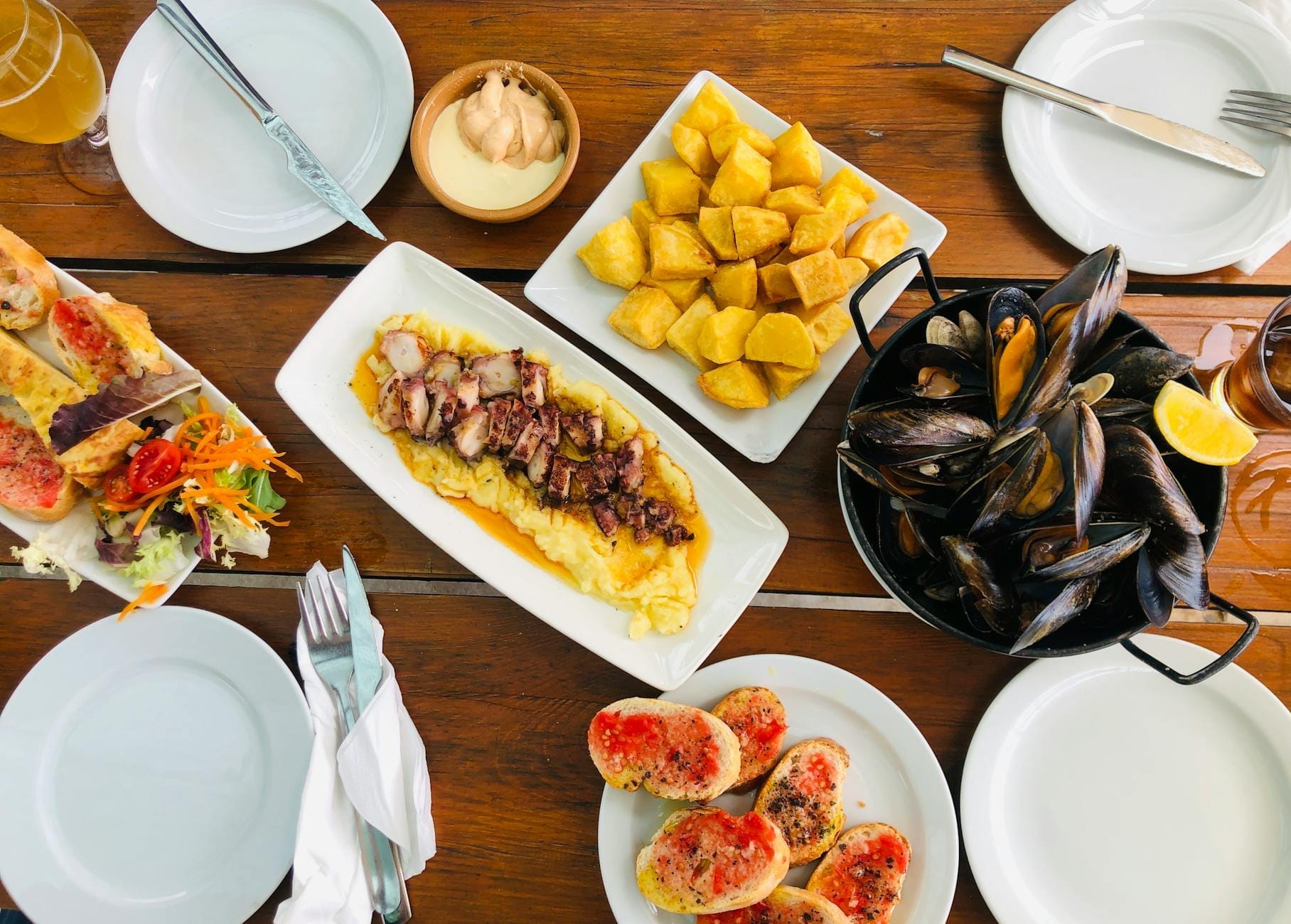 Overhead view of a table with several Catalan dishes including pan con tomate, grilled octopus, mussels, patatas bravas, and salad.