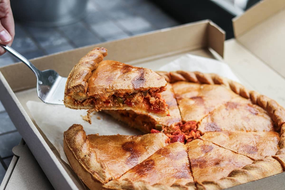 Una pizza Chicago deep dish in una scatola aperta, con una fetta sollevata per rivelare il ripieno spesso e a strati.