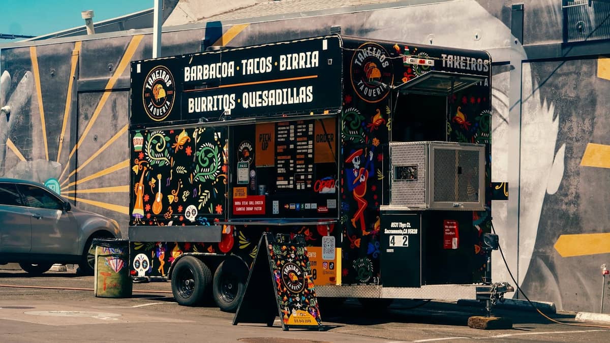 Colorato food truck di tacos parcheggiato in un parcheggio urbano, con murales di ispirazione messicana e un'auto vicina alla luce del giorno.