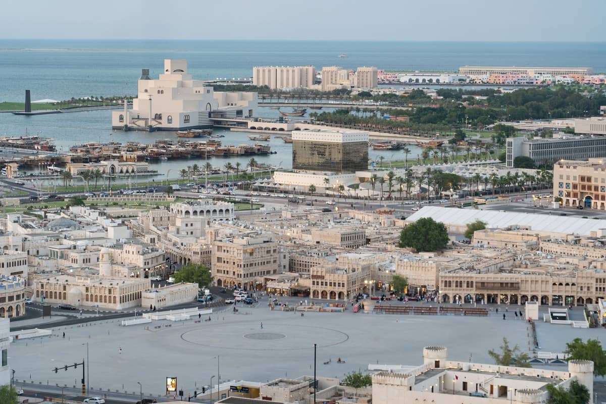 Luftaufnahme der markanten Stadtteile Dohas, darunter Souq Waqif und die Uferpromenade, die die vielfältige städtische Landschaft der Stadt zeigen.