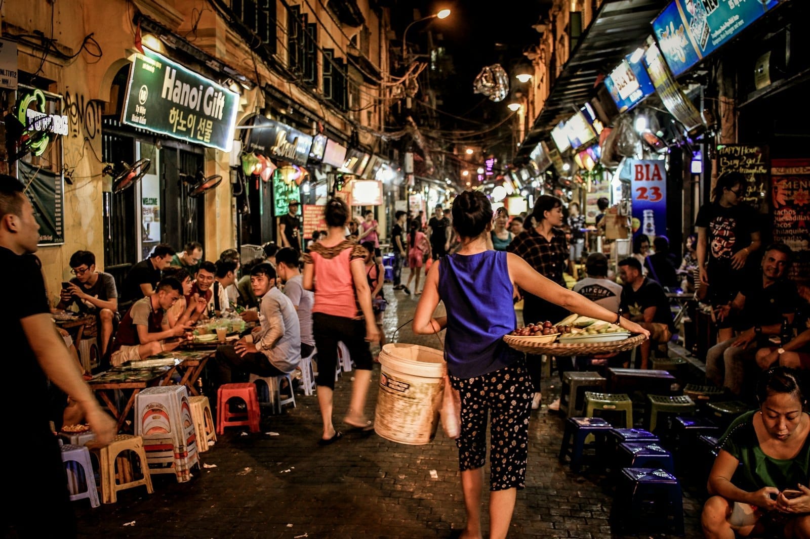 Bustling Hanoi night street food scene with many locals and tourists dining on small stools, vibrant lights, and food vendors serving amid lively atmosphere.