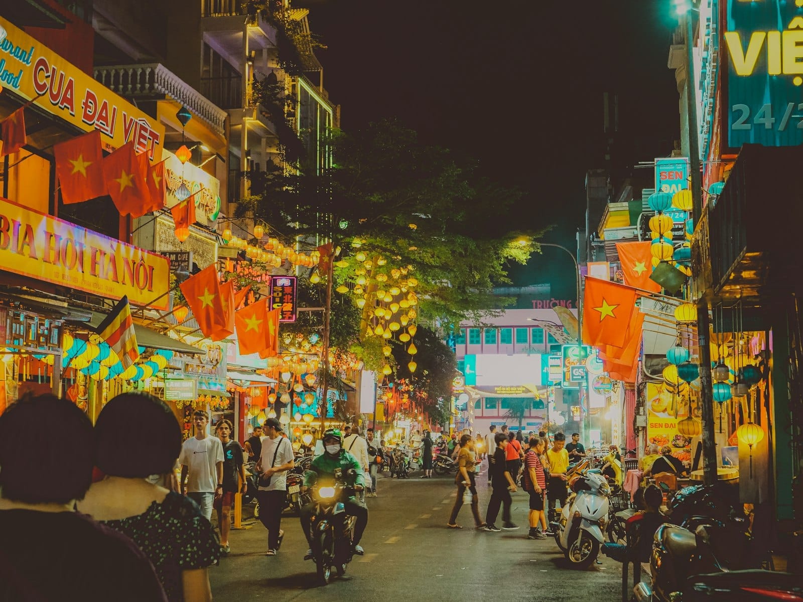Calle animada de Ho Chi Minh City de noche, con letreros de neón, peatones, motocicletas y restaurantes iluminados que reflejan la vibrante escena gastronómica de la ciudad.