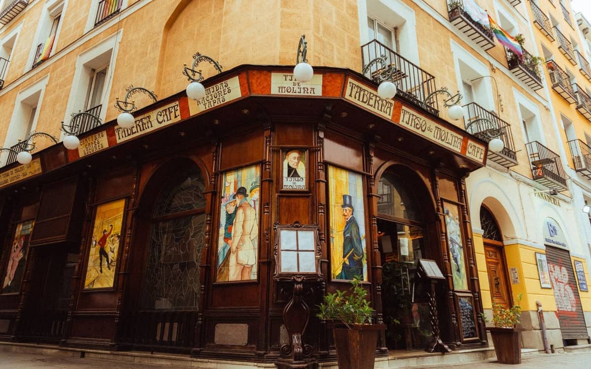 Vista de esquina de una taberna tradicional de Madrid con fachada de madera, letreros históricos y ventanas pintadas en una encantadora calle antigua.