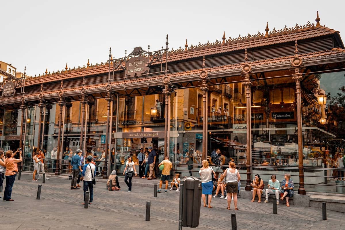 Vista exterior del Mercado de San Miguel en Madrid con personas reunidas afuera, reflejando la vibrante escena gastronómica y la cultura de mercado.