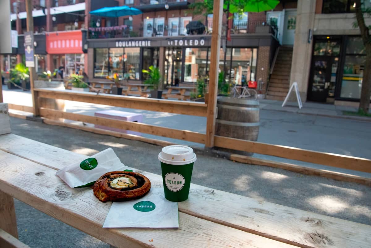 Kaffee und Gebäck auf einem Tisch im Freien mit Fassaden einer Boulangerie in Montréal und urbanem Patio im Hintergrund