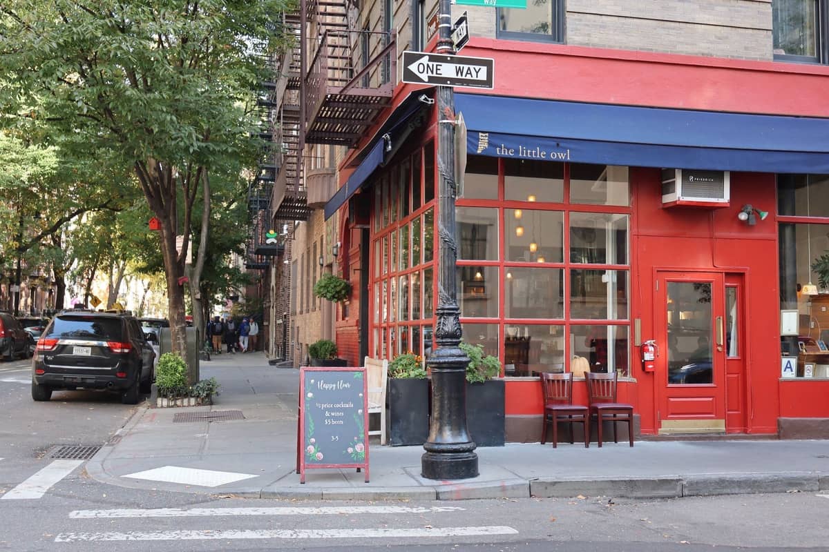 Ein gemütliches Restaurant in New York City an einer Straßenecke mit blauer Markise, roter Fassade und einer Kreidetafel-Speisekarte draußen.