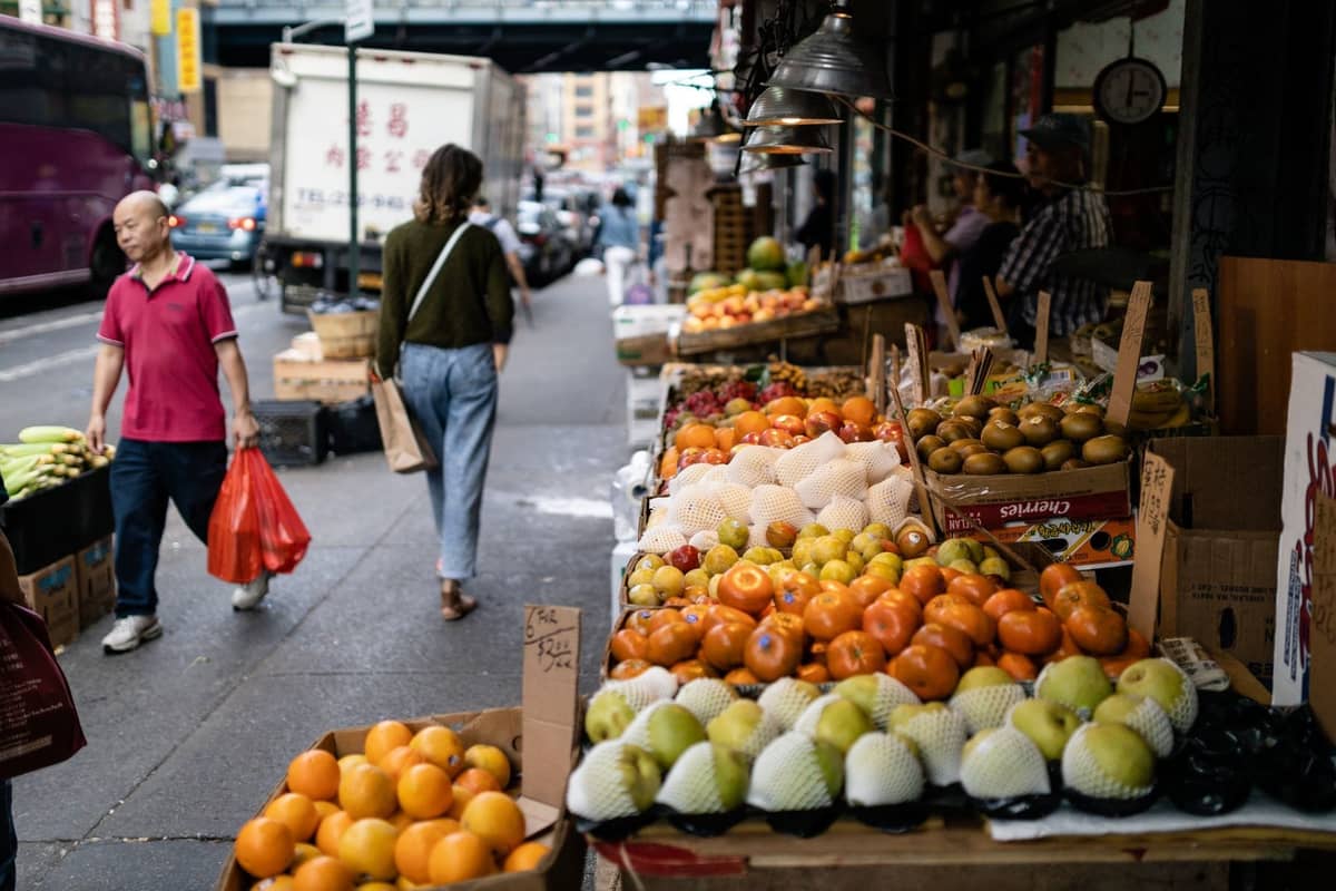 Freiluft-Markt mit frischen Produkten auf einer belebten Straße in New York City, mit ausgestelltem frischem Obst und einkaufenden Menschen.