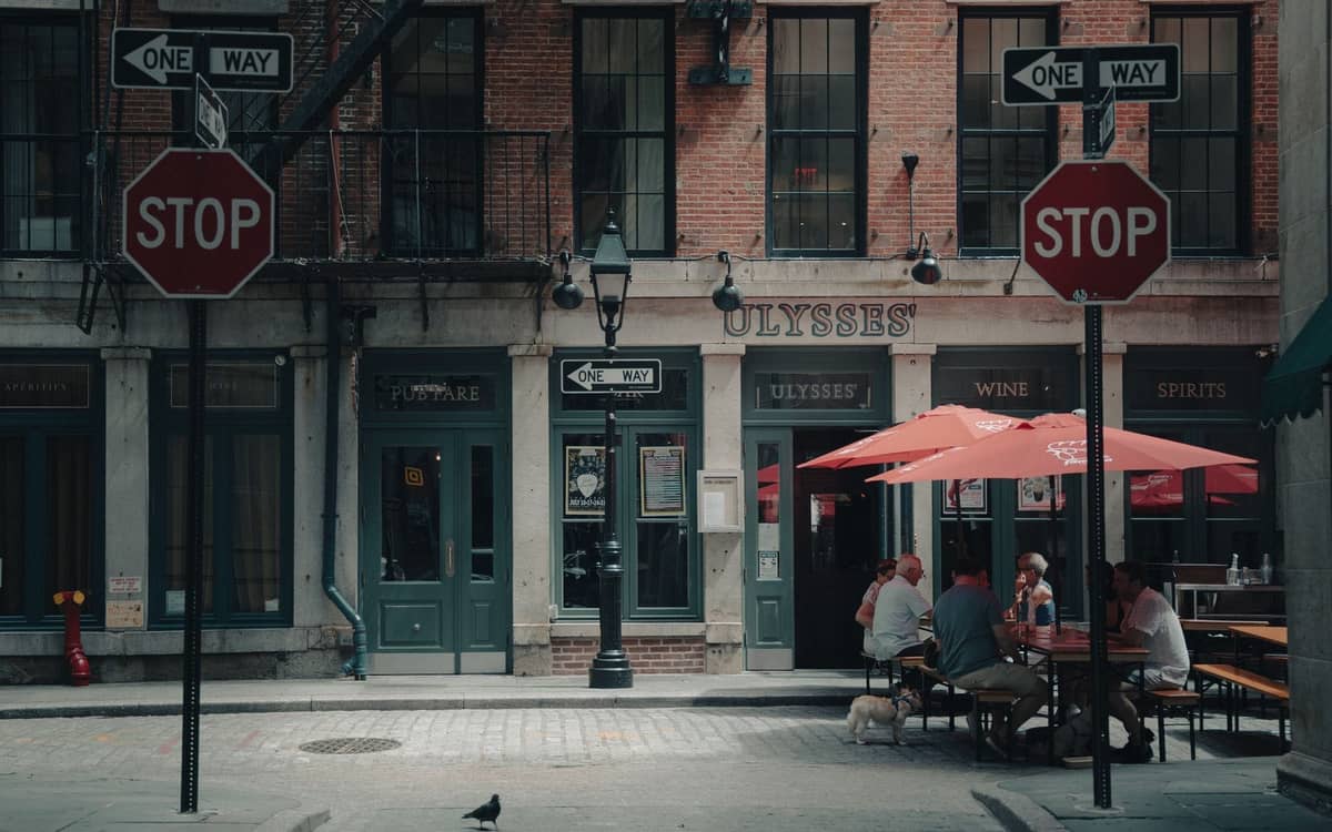 Menschen beim Essen im Freien in einem Restaurant unter einem roten Sonnenschirm auf einer Straße in New York City mit klassischen Backsteingebäuden.