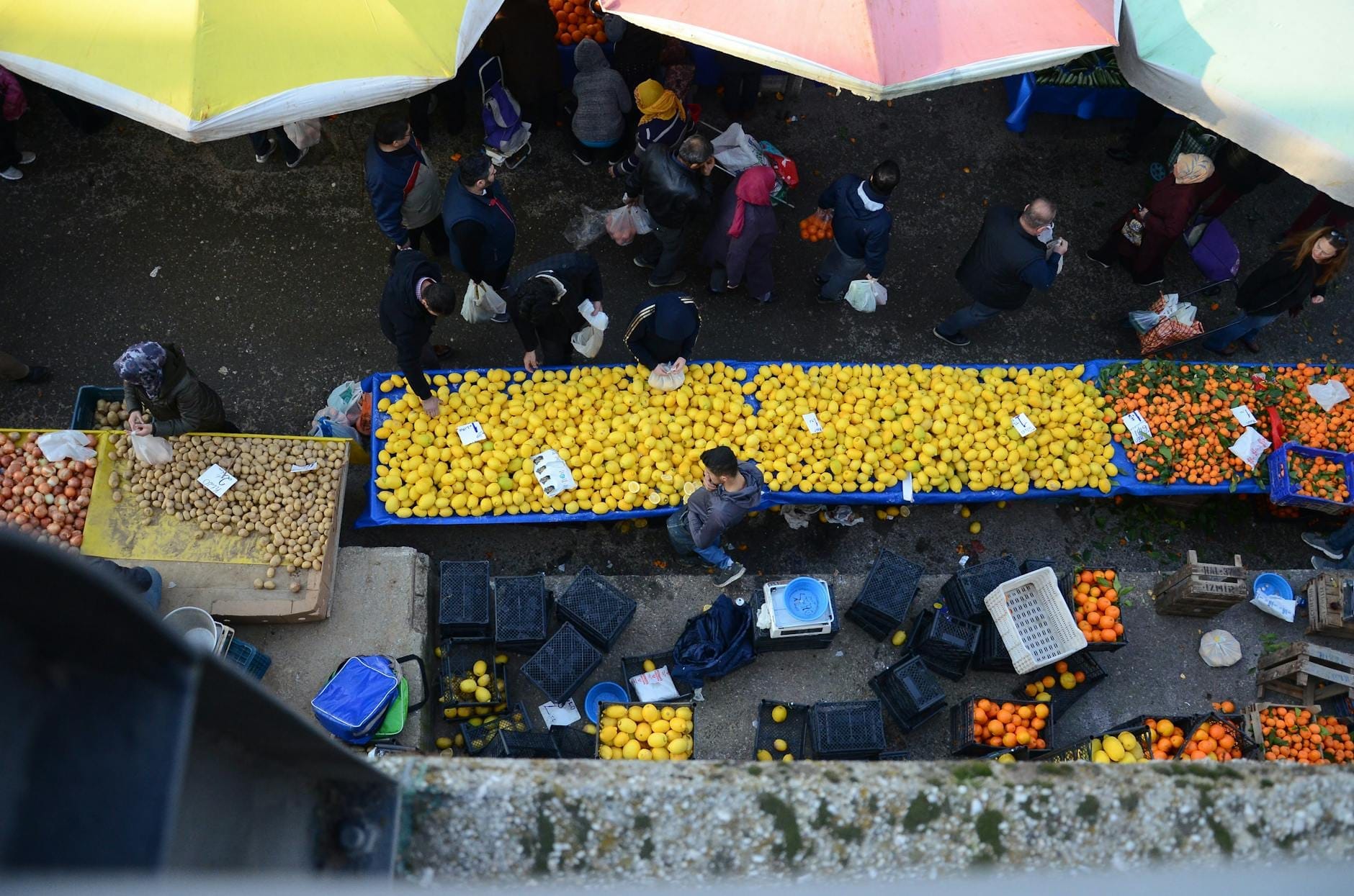 Vogelperspektive auf einen belebten Freiluftmarkt in Paris mit Menschen, die an bunten Obst- und Gemüseständen unter Sonnenschirmen einkaufen.
